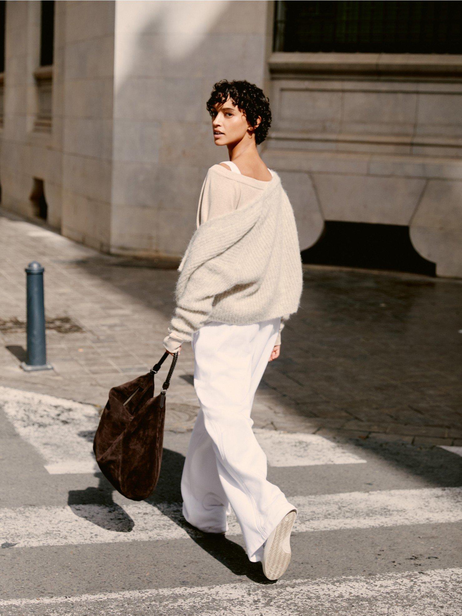 a woman in white pants and sweater crossing a street