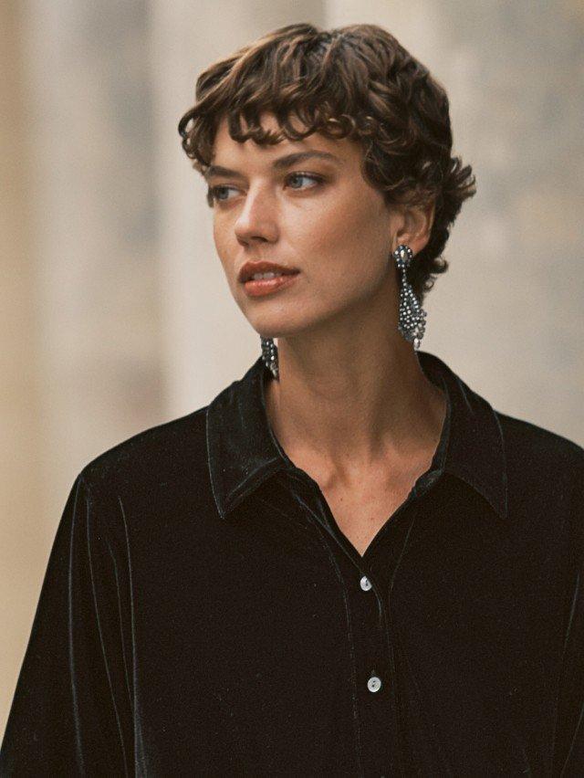 a woman with short hair wearing a black shirt and earrings