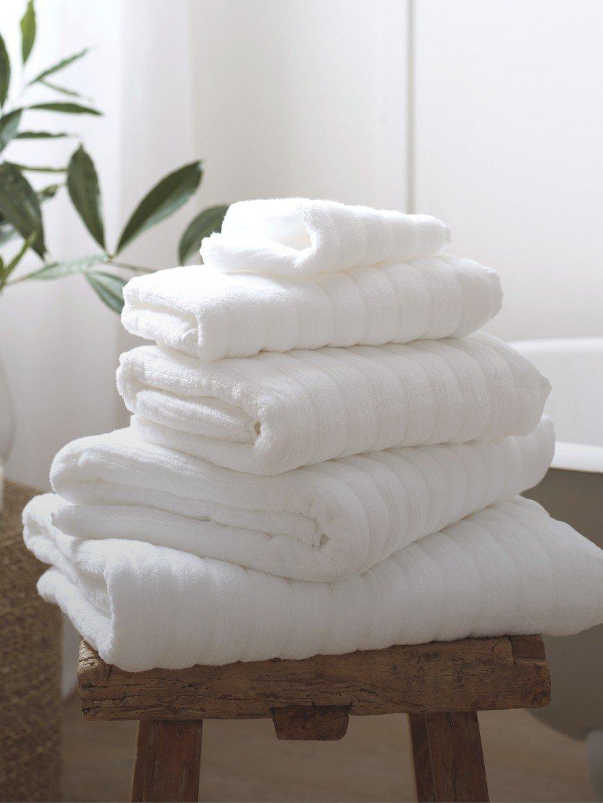 a stack of white towels sitting on a stool next to a plant