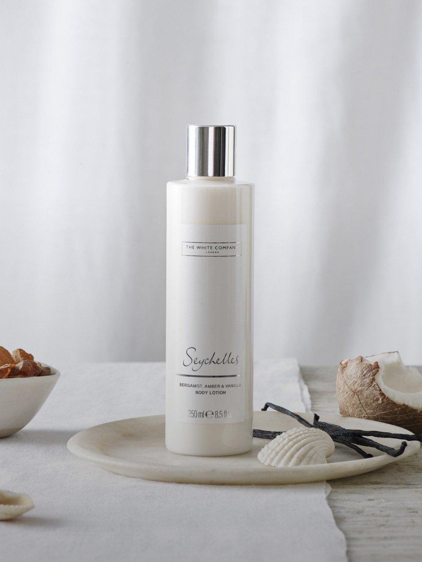 a bottle of lotion on a plate next to a bowl of shells