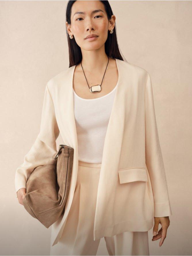 a woman in a white blazer and white pants holding a brown purse