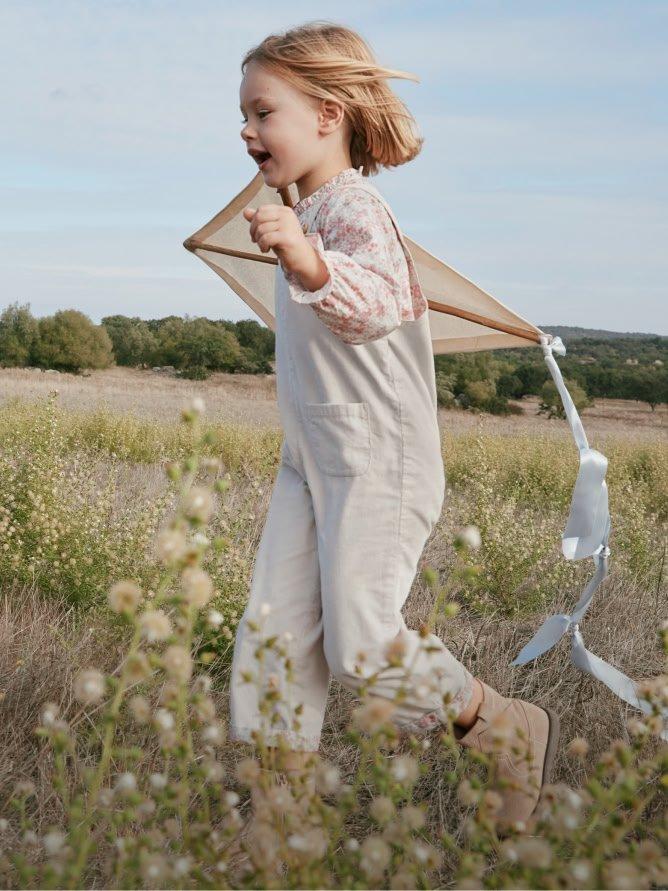 a little girl running through a field with a kite