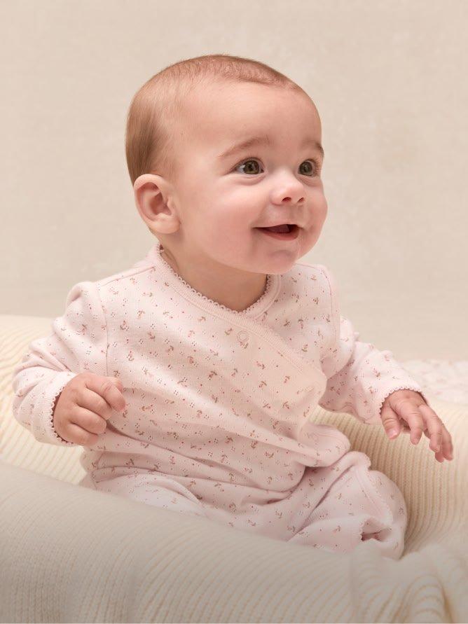 a baby in a pink outfit sitting on a white bed